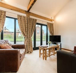 A living room with two leather sofas a small wooden coffee table and a television by glass doors with curtains at Partridge in Wheatacre