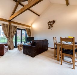 A living room with leather sofas a wooden dining table and chairs with curtains on windows at Partridge in Wheatacre