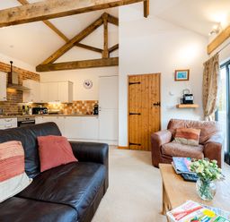 A living room with leather sofas wooden coffee table and an open kitchen with white cabinets at Partridge in Wheatacre