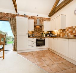 A kitchen with white cabinets tiled floor and wooden dining table near glass door at Partridge in Wheatacre