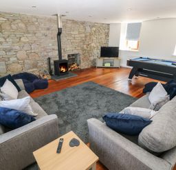 A living room with two gray sofas a wood burning stove a television and a pool table at Dalton Cottage in Llansaint