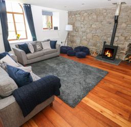 A living room with grey sofas a stone wall and a wood burning stove at Dalton Cottage in Llansaint