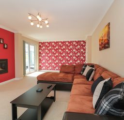 A living room with a brown sectional sofa black coffee table and patterned red wallpaper at Te Papa in North Petherton