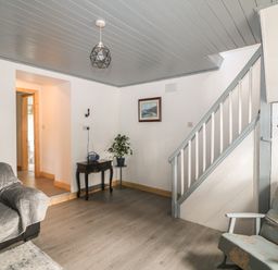 A living room with a sofa covered with a grey quilted cover a floral armchair a small table with a radio and a plant a framed picture on the wall and a staircase at Curragh Cottage Rathimney near New Ross County Wexford