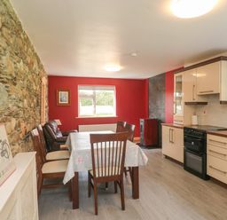 A kitchen dining area with a wooden table and chairs stone wall and modern kitchen at Curragh Cottage Rathimney near New Ross County Wexford