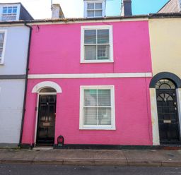 A street view of three connected houses with a pink middle house with black door and white window frames at Georgian Hideaway in Weymouth