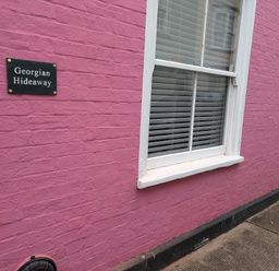 A pink brick wall with a window and a sign reading Georgian Hideaway at Georgian Hideaway in Weymouth