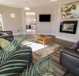 A living room with leather sofas a wooden coffee table a wall-mounted TV an electric fireplace and a large window at Moorhen House in Loughanure near Annagry County Donegal