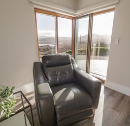 A room with a black leather armchair next to a glass side table with a plant by large windows at Moorhen House in Loughanure near Annagry County Donegal