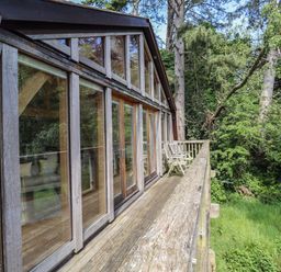 A wooden balcony with two chairs outside large glass doors surrounded by trees at The Boathouse in Belford
