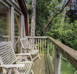 A wooden balcony with two wooden chairs and glass railing overlooking green trees at The Boathouse in Belford