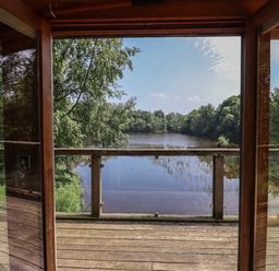 A wooden balcony overlooking a lake surrounded by trees at The Boathouse in Belford