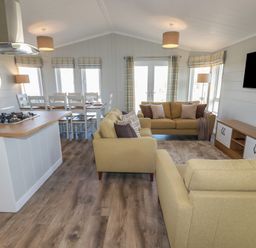 An open plan living and dining area with beige sofas a dining table and kitchen island at 4 Meadow Retreat in Dobwalls