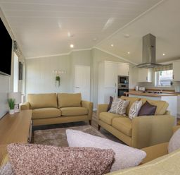A living room with yellow sofas a wooden cabinet a wall mounted tv and an open kitchen at 4 Meadow Retreat in Dobwalls