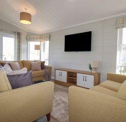 A living room with two yellow sofas, a TV mounted on the wall, and a wooden cabinet at 4 Meadow Retreat in Dobwalls
