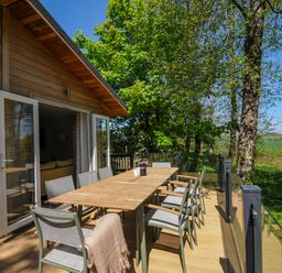 An outdoor wooden deck with a long table and chairs near a wooden house and trees at 23 Meadow Retreat in Dobwalls