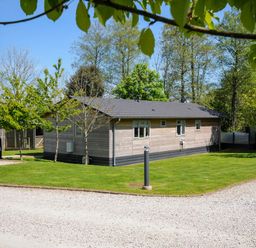 A wooden single-story house with a tiled roof on a grassy area with trees at 23 Meadow Retreat in Dobwalls
