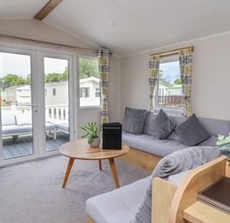 A living room with a round wooden table gray sofas and patio doors at Windermere Lodge in Morecambe