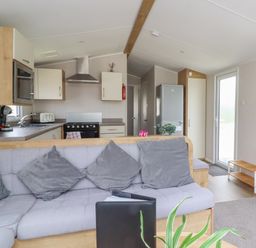 A kitchen and living area with a grey cushioned sofa and grey pillows at Windermere Lodge in Morecambe