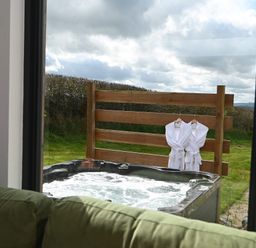 A bubbling outdoor hot tub with two white robes hanging on a wooden fence behind it at Cae Pren in New Mills near Llanfair Caereinion