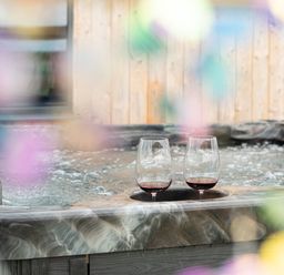 A hot tub with two glasses of red wine at Cae Pren in New Mills near Llanfair Caereinion