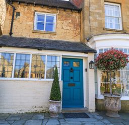 Front of a stone and brick house with blue door and potted plants outside at Broadway Cottage in Broadway