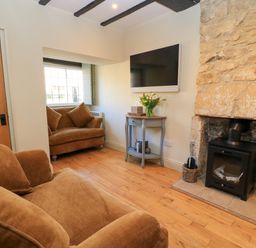 A living room with brown sofas a stone fireplace a wall mounted TV and a window at Broadway Cottage in Broadway