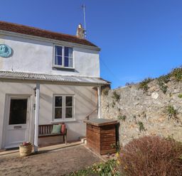 The exterior of a two-story house with a wooden bench near the door and a stone wall beside it at 4 Lymbrook Cottages in Lyme Regis