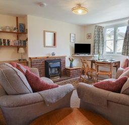 A living room with sofas, a dining table set, a TV, and a fireplace at 4 Lymbrook Cottages in Lyme Regis