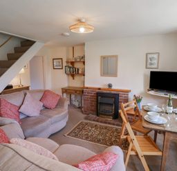 A living room with sofas a dining table set with dishes a television and a fireplace at 4 Lymbrook Cottages in Lyme Regis