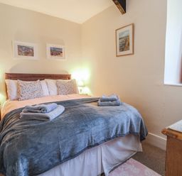 A bedroom with a double bed with towels on the blanket bedside tables with lamps and framed pictures on the walls at 4 Lymbrook Cottages in Lyme Regis