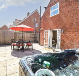A patio with a hot tub table with umbrella and chairs and open doors leading to a living room at The Old Chapel in Foxley near Bawdeswell
