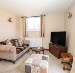 A living room with sofa cushions a patchwork ottoman a television on a wooden chest and a small side table at The Old Chapel in Foxley near Bawdeswell