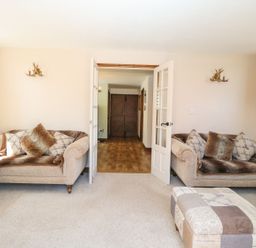 A living room with two beige sofas and an ottoman facing double glass doors at The Old Chapel in Foxley near Bawdeswell