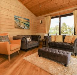 A living room with two grey sofas a beige armchair a long grey ottoman and a large window at Moonlake Lodge in Woolsery near Woolfardisworthy