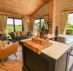 An open-plan kitchen and living area with a kitchen island with snacks on it and sofas near large windows at Moonlake Lodge in Woolsery near Woolfardisworthy