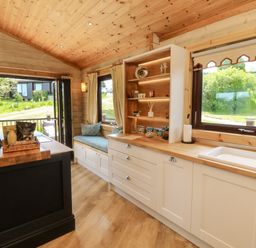 A kitchen with white cabinets wooden countertops a sink window seating area and open patio doors at Moonlake Lodge in Woolsery near Woolfardisworthy