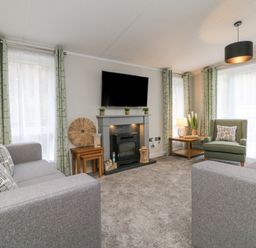 A living room with two gray sofas a green armchair a fireplace and a wall mounted tv at 18 Manleigh Park in Combe Martin