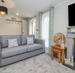 A living room with a grey sofa two patterned cushions wooden nesting tables a fireplace and a mounted television at 18 Manleigh Park in Combe Martin