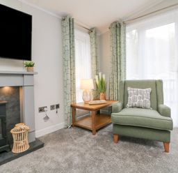 A living area with a green armchair, side table with a lamp, fireplace, and television at 18 Manleigh Park in Combe Martin