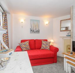 A living room with a red sofa and patterned cushions next to a white table with a television on it at Sea Pinks in Looe