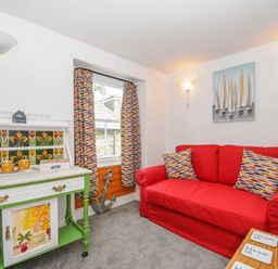 A room with a red sofa cushions curtain and a table with a yellow kettle and cups at Sea Pinks in Looe