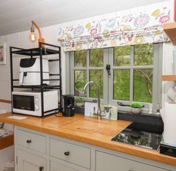 A kitchen counter with a sink microwave kettle and air fryer under a window at Burr 2 Shepherds Hut Swimbridge near Barnstaple