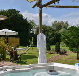 An outdoor area with a hot tub a wooden deck chairs hammock and umbrella at Burr 2 Shepherds Hut in Swimbridge near Barnstaple