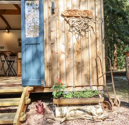 An outdoor area with a wooden door and flower bed at Tanglewood Shepherds Hut in Welshpool