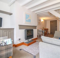 A living room with a TV on a cabinet a fireplace sofas and a dining table at Cobblestone Cottage in Bude