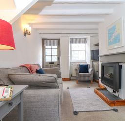 A sitting room with a gray sofa a red lamp a plaid armchair a rug a fireplace and a television at Cobblestone Cottage in Bude