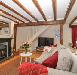 A living room with a wood burning stove a sofa a coffee table with flowers and wooden beams on the ceiling at 4 Barton Cottages in Down Thomas near Plymouth