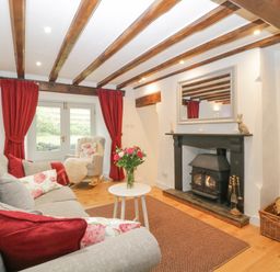 A living room with a grey sofa red curtains a rocking chair and a fireplace at 4 Barton Cottages Down Thomas near Plymouth