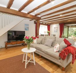 A living room with a gray sofa and red curtains near a dining table and TV at 4 Barton Cottages in Down Thomas near Plymouth